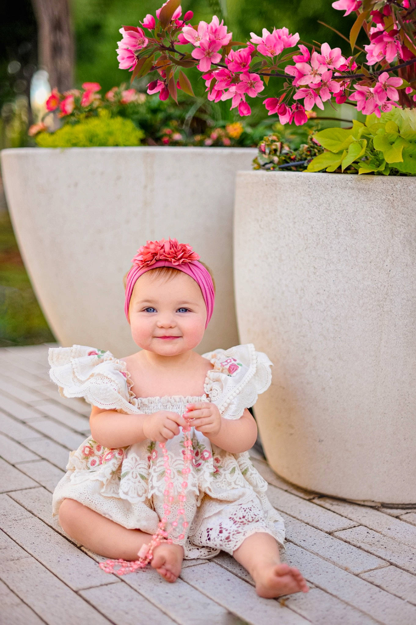 Lola is registered to the contest to win money with this photo: baby, baby_toddler_clothing, beauty, child, dress, flower, grass, happy, headband, headgear, headpiece, headwear, joy, magenta, person, petal, pink, plant, sitting, skin