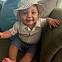 baby, child, smiling, hat, striped_clothing, shorts, couch, pillows, indoor, happy, portrait, sitting, skin, face, hand, foot, home, cute, infant, cozy