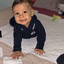 toddler, child, smiling, crawling, bed, quilt, indoors, face, hands, clothing, black_shirt, happy, cute, young_child, person, portrait, baby, skin, eyes, hair