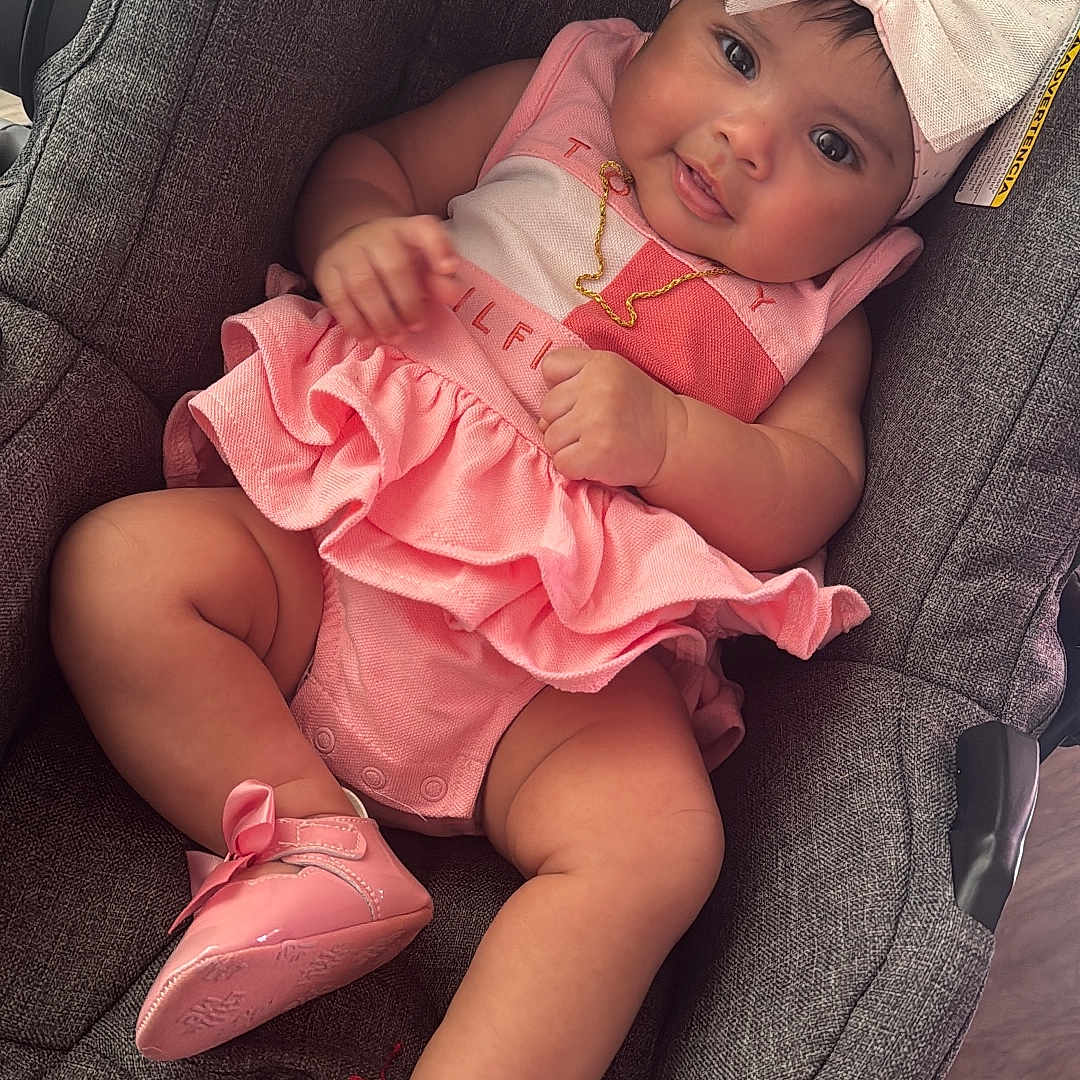 Samary is registered to the contest to win money with this photo: accessory, baby, bow, car_seat, child, clothing, cute, floor, footwear, gold_necklace, gray_car_seat, headband, indoors, infant, person, pink_dress, pink_shoes, portrait, sitting, smiling