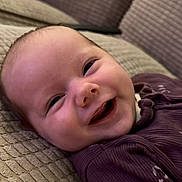 Harriet joined the competition — help win amazing prizes! baby, child, close_up, couch, cozy, cute, fabric, face, happy, head, indoor, infant, lying_down, person, portrait, purple_clothing, relaxed, skin, smiling, texture