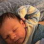 baby, newborn, sleeping, pajamas, striped_clothing, blanket, soft_texture, peaceful, infant, cute, face, head, skin, resting, cozy, child, person, indoors, closeup, portrait