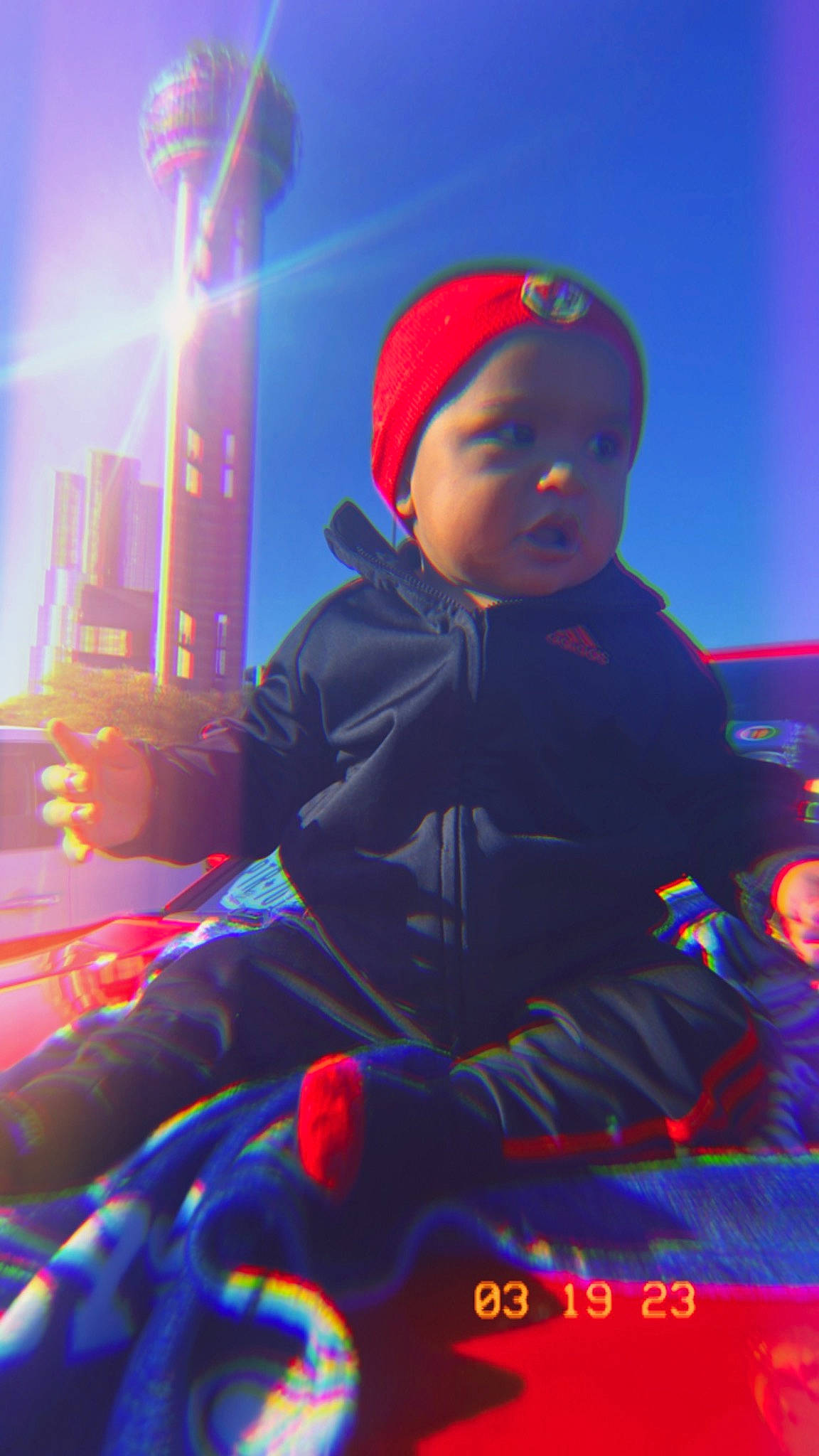 Edward is registered to the contest to win money with this photo: automotive_lighting, baby, cap, child, cloud, electric_blue, event, fun, headwear, holiday, leisure, lens_flare, magenta, person, personal_protective_equipment, recreation, sitting, sky, standing, toddler