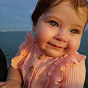 Nova joined the competition — help win amazing prizes! baby, child, face, blue_eyes, smile, peach_clothing, ruffles, sunlight, outdoor, water, portrait, cute, happy, skin, hand, person, infant, cheeks, young, natural_light