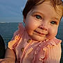 baby, child, face, blue_eyes, smile, peach_clothing, ruffles, sunlight, outdoor, water, portrait, cute, happy, skin, hand, person, infant, cheeks, young, natural_light