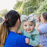 Athena joined the competition — help win amazing prizes! baby, background, bow, casual_clothing, child, daylight, family, greenery, hair_tie, happy, headband, holding, nature, outdoor, people, person, portrait, smile, toddler, woman
