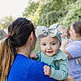baby, background, bow, casual_clothing, child, daylight, family, greenery, hair_tie, happy, headband, holding, nature, outdoor, people, person, portrait, smile, toddler, woman