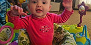 Athena is registered to the contest to win money with this photo: baby, child, infant, pink_shirt, activity_center, toys, smiling, arms_up, living_room, lamp, photoframes, curtains, carpet, furniture, home_interior, play, fun, happy, face, person