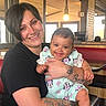 woman, baby, smiling, tattoos, short_hair, indoor, restaurant, light_bulb, table, chair, holding, cute, happy, person, clothing, face, portrait, child, infant, casual