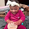 baby, infant, child, headband, bow, smile, pink_clothing, milestone, wooden_plaque, hand, blanket, soft_focus, indoor, happy, sitting, portrait, cute, celebration, person, toddler