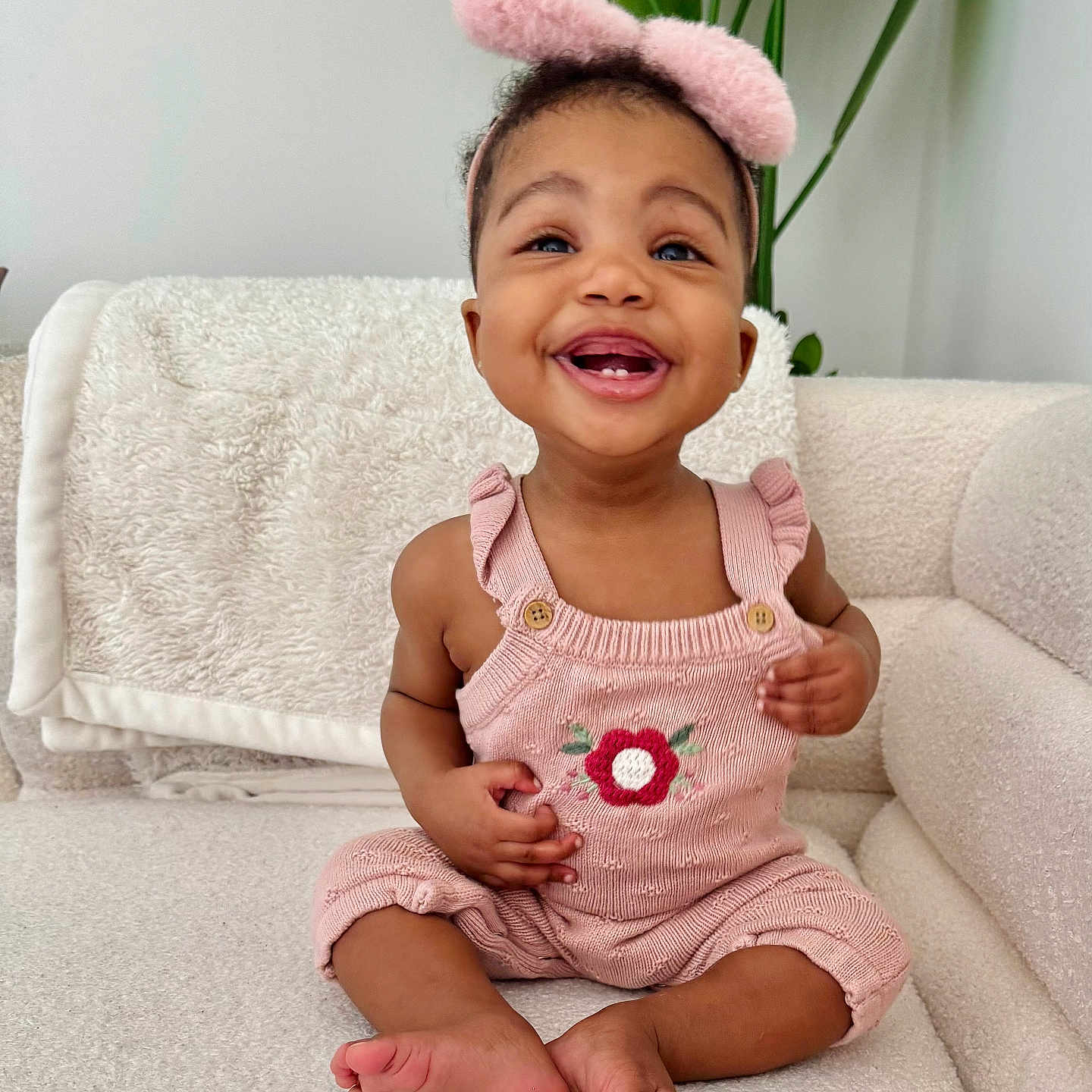 Lomankosi is registered to the contest to win money with this photo: baby, blanket, child, couch, cozy, cute, flower, furniture, happy, headband, home, indoors, knitted, pink_clothing, plant, portrait, sitting, smiling, toddler, toes