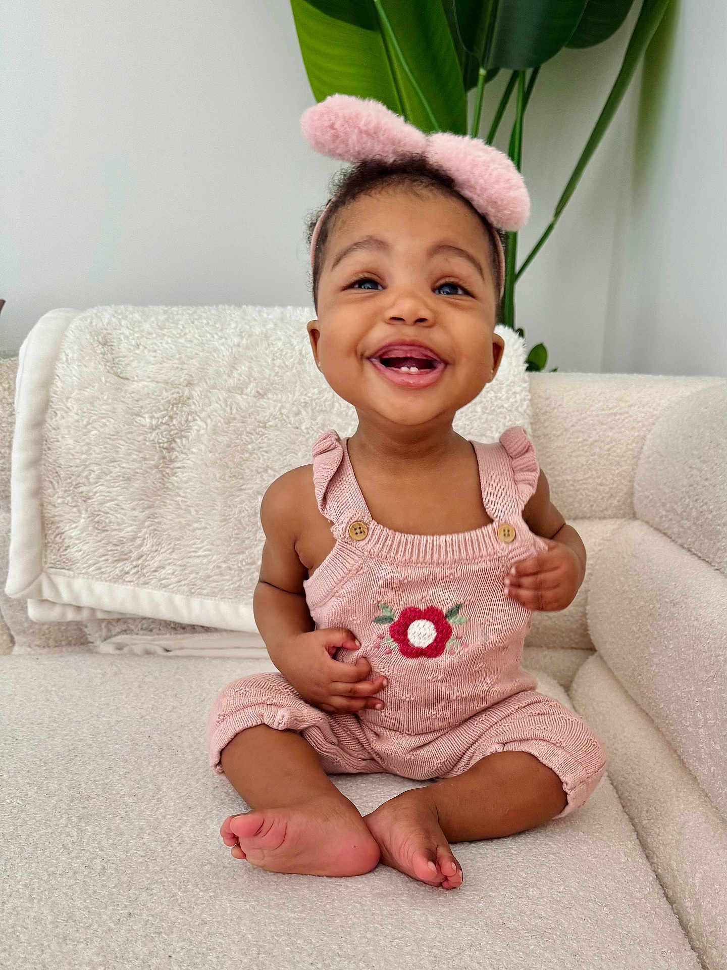 Lomankosi is registered to the contest to win money with this photo: baby, blanket, child, couch, cozy, cute, flower, furniture, happy, headband, home, indoors, knitted, pink_clothing, plant, portrait, sitting, smiling, toddler, toes