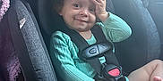 Luna is registered to the contest to win money with this photo: toddler, child, car_seat, curly_hair, smile, hand_on_face, seat_belt, car_interior, window, clothing, green_sweater, baby, sitting, safety, cute, indoors, daylight, happy, person, seat