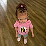 toddler, child, curly_hair, pink_shirt, bee_happy, shorts, standing, wooden_floor, indoors, looking_up, footwear, casual_clothing, cute, small_person, person, hair_accessories, happy_message, flooring, smiling, young_child