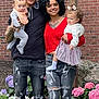 Luna is registered to the contest to win money with this photo: family, man, woman, child, toddler, baby, brick_wall, wooden_cross, flowers, garden, grass, ripped_jeans, sneakers, curly_hair, smiling, outdoor, portrait, holding, casual_clothing, happy
