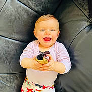 Charline participe au concours pour gagner de l'argent avec cette photo : baby, child, smiling, sitting, toy, black_leather_couch, colorful_pants, floral_pattern, happy, person, indoor, playful, cute, bright_eyes, holding_object, young_child, portrait, casual_clothing, comfortable, fun