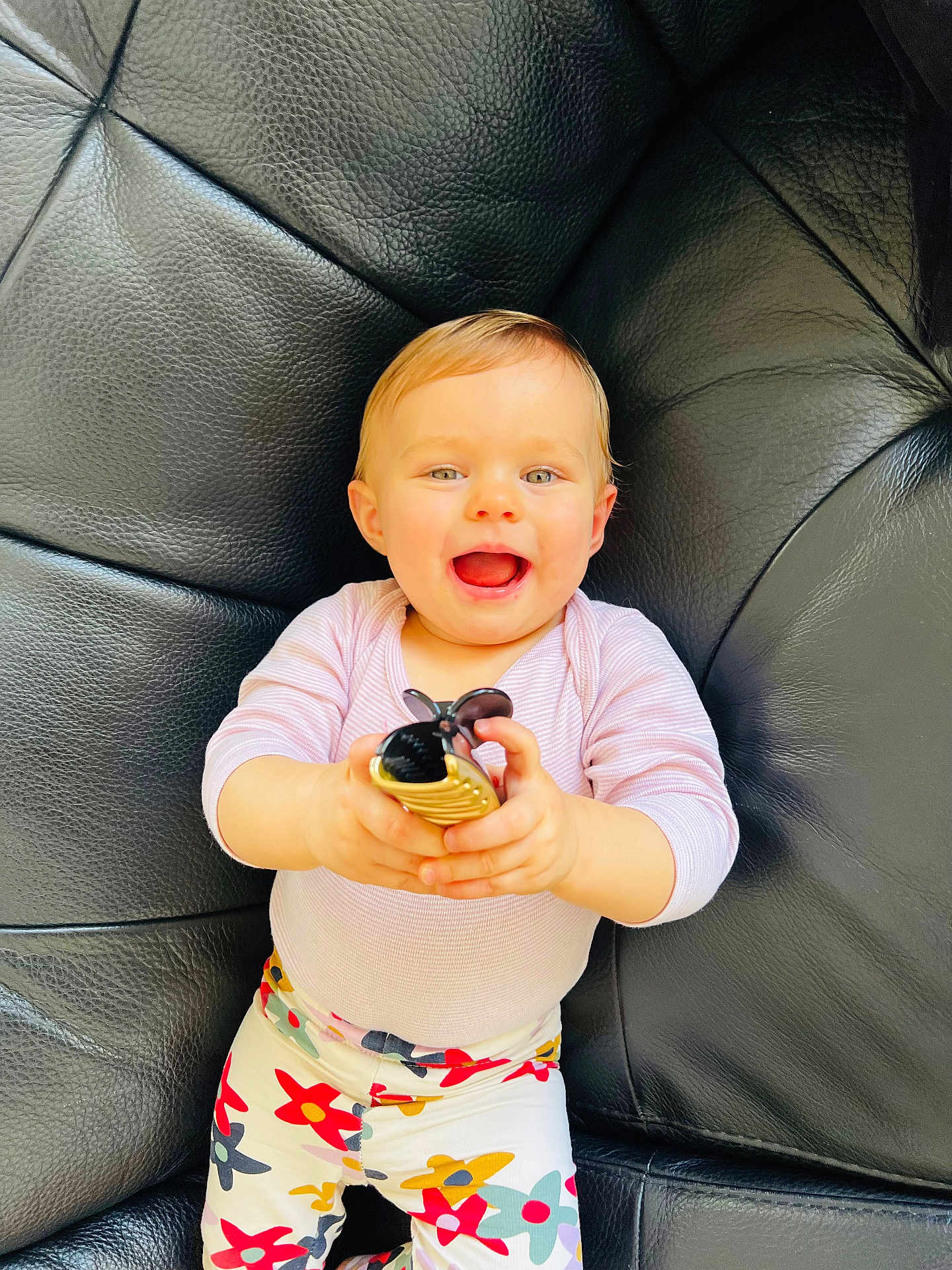 Charline participe au concours pour gagner de l'argent avec cette photo : baby, child, smiling, sitting, toy, black_leather_couch, colorful_pants, floral_pattern, happy, person, indoor, playful, cute, bright_eyes, holding_object, young_child, portrait, casual_clothing, comfortable, fun