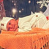 baby, infant, knitted_hat, knitted_outfit, orange_blanket, winter_decorations, snowflake, gift_box, holiday_theme, cozy, cute, portrait, lying_down, soft_lighting, child, newborn, warm_colors, indoors, festive, smiling