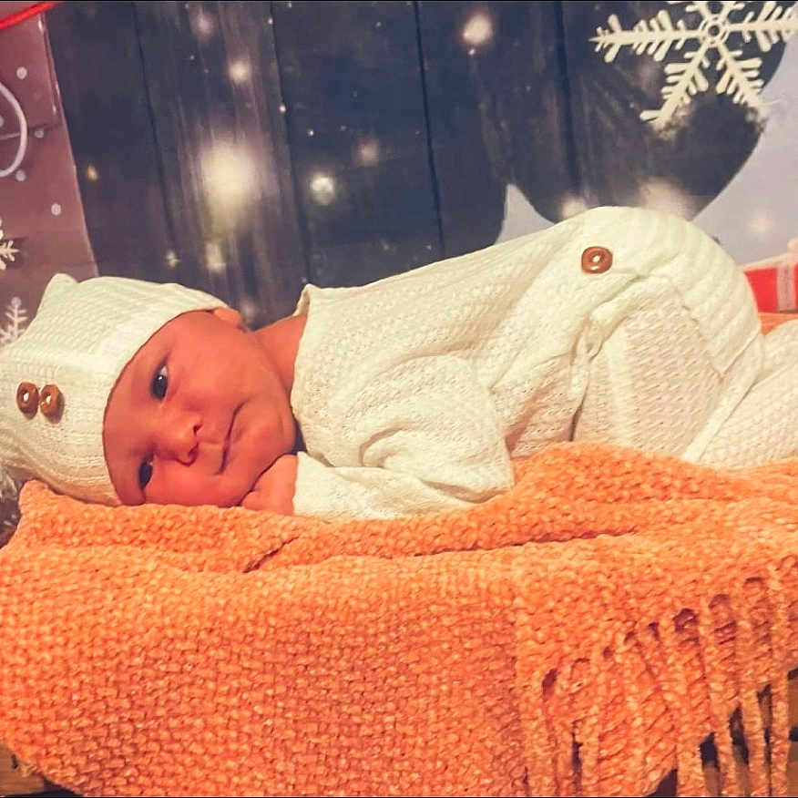 Scarlet is registered to the contest to win money with this photo: baby, infant, knitted_hat, knitted_outfit, orange_blanket, winter_decorations, snowflake, gift_box, holiday_theme, cozy, cute, portrait, lying_down, soft_lighting, child, newborn, warm_colors, indoors, festive, smiling