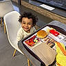 Hezekiah is registered to the contest to win money with this photo: apple_slices, burger, child, curly_hair, fast_food, food, fries, happy, indoor, meal, napkin, person, restaurant, seat, smiling, table, toddler, tray, white_chair, window