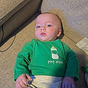 Zoey is registered to the contest to win money with this photo: baby, infant, child, person, face, portrait, sofa, couch, green_shirt, pint_sized, bottle_graphic, home_interior, pants, hand, eyes, looking_up, relaxed, cozy, textured_fabric, casual