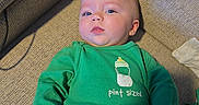 Zoey is registered to the contest to win money with this photo: baby, bottle_graphic, casual, child, couch, cozy, eyes, face, green_shirt, hand, home_interior, infant, looking_up, pants, person, pint_sized, portrait, relaxed, sofa, textured_fabric