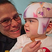 Zoey is registered to the contest to win money with this photo: adult, baby, child, glasses, helmet, pacifier, person, smile, face, closeup, indoor, holding, apparel, headgear, cute, toddler, love, family, interaction, portrait