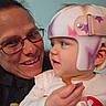 adult, baby, child, glasses, helmet, pacifier, person, smile, face, closeup, indoor, holding, apparel, headgear, cute, toddler, love, family, interaction, portrait