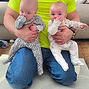 Chloe joined the competition — help win amazing prizes! baby, infant, child, person, adult, holding, thumb_sucking, onesie, polka_dots, floral_pattern, bright_shirt, jeans, indoor, living_room, couch, floor_mat, hand, kneeling, cute, home
