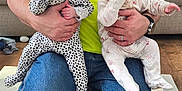 Chloe joined the competition — help win amazing prizes! baby, infant, child, person, adult, holding, thumb_sucking, onesie, polka_dots, floral_pattern, bright_shirt, jeans, indoor, living_room, couch, floor_mat, hand, kneeling, cute, home