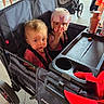 toddler, child, stroller, helmet, snack, bottle, double_stroller, outdoor, people, legs, concrete_floor, clothing, seat, baby, protective_gear, red, black, pink, person, casual