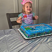 Alaina joined the competition — help win amazing prizes! birthday, cake, celebration, chair, child, costume, crown, dessert, food, happy, icing, indoor, mermaid, party_banner, plastic_tablecloth, portrait, smile, sprinkles, table, toddler