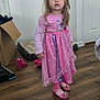boots, cardboard_box, child, costume, curious, door, face_paint, floor, girl, home, indoor, long_hair, pet_bed, pink_dress, playful, princess, standing, tiara, toy, wooden_floor