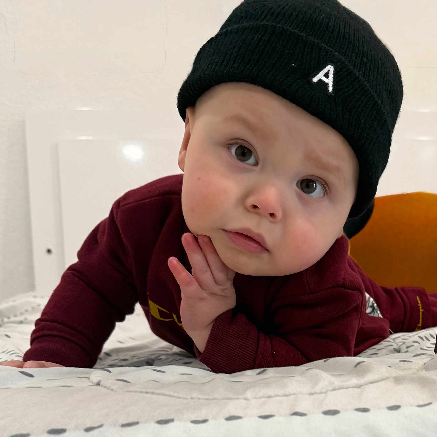 Anthuan is registered to the contest to win money with this photo: baby, beanie, bed, blanket, casual, child, clothing, cozy, curious, expression, face, hand, hat, indoor, looking, maroon, person, portrait, resting, young_child
