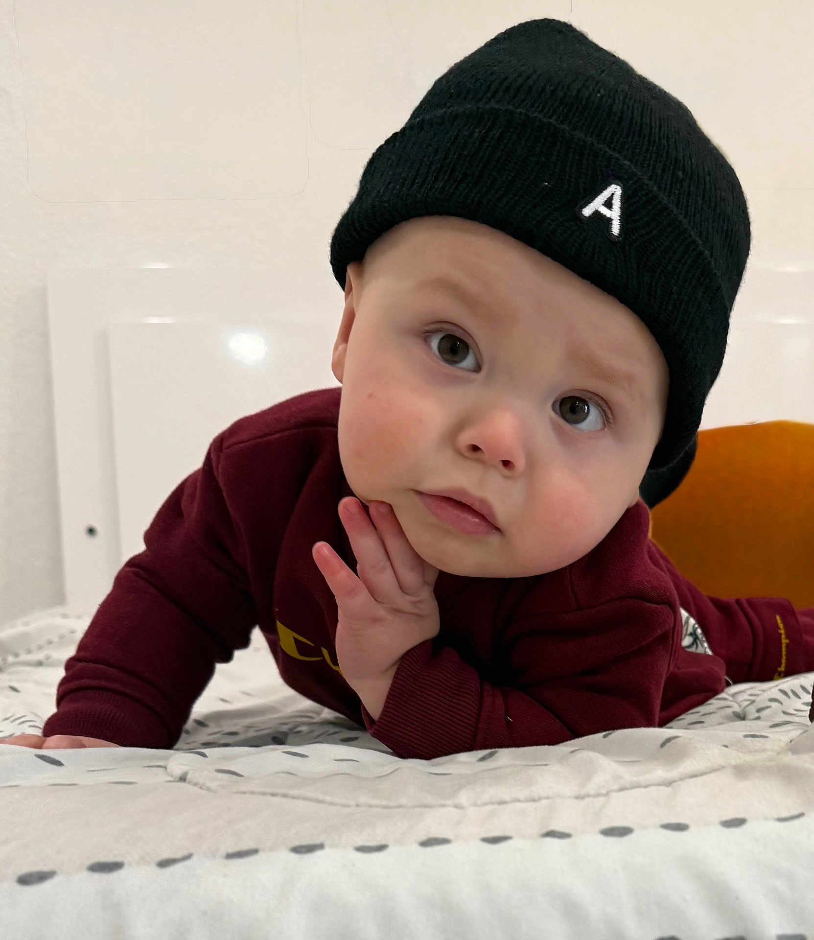 Anthuan is registered to the contest to win money with this photo: baby, child, face, beanie, hat, clothing, maroon, bed, blanket, hand, portrait, indoor, expression, curious, looking, person, young_child, cozy, casual, resting