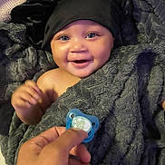 Ziyah joined the competition — help win amazing prizes! baby, smiling, blanket, black_bonnet, pacifier, hand, blue_eyes, soft_texture, happy, infant, wrapped, cozy, indoor, portrait, cute, child, face, skin, comfort, joy