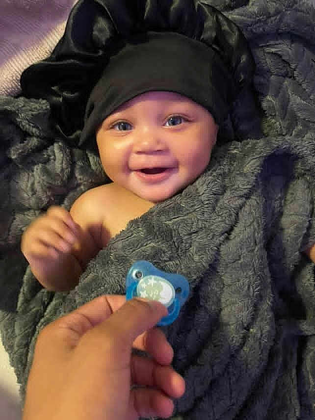 Ziyah joined the competition — help win amazing prizes! baby, smiling, blanket, black_bonnet, pacifier, hand, blue_eyes, soft_texture, happy, infant, wrapped, cozy, indoor, portrait, cute, child, face, skin, comfort, joy