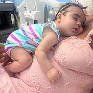 Trinity is registered to the contest to win money with this photo: baby, sleeping, child, person, striped_clothing, pink_dress, headband, indoor, play_kitchen, wall_decals, fish, cozy, resting, infant, hand, face, soft_light, room, close_up, cute