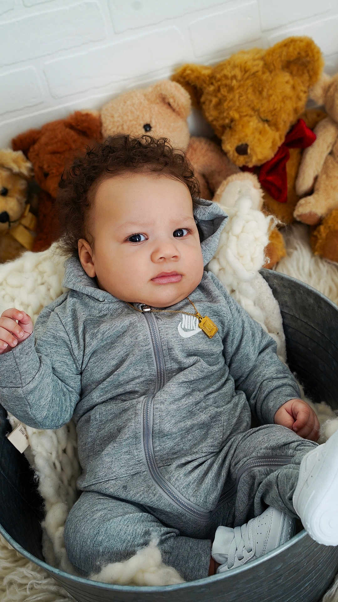 Myles is registered to the contest to win money with this photo: baby, child, teddy_bear, plush_toy, gray_tracksuit, nike_logo, metal_tub, blanket, curly_hair, white_shoes, indoor, portrait, cute, infant, soft_texture, cozy, expression, person, sitting, toy