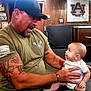 Miles is registered to the contest to win money with this photo: man, baby, tattoo, cap, restaurant, table, food, plate, wood_paneling, sports_memorabilia, interaction, curiosity, casual, seated, beard, short_sleeve_shirt, infant, smile, person, indoor