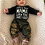 baby, smiling, infant, clothing, black_shirt, text, camo_pants, booties, blanket, soft_texture, happy, cute, lying_down, indoor, child, portrait, small_hands, cheerful, infant_fashion, cozy