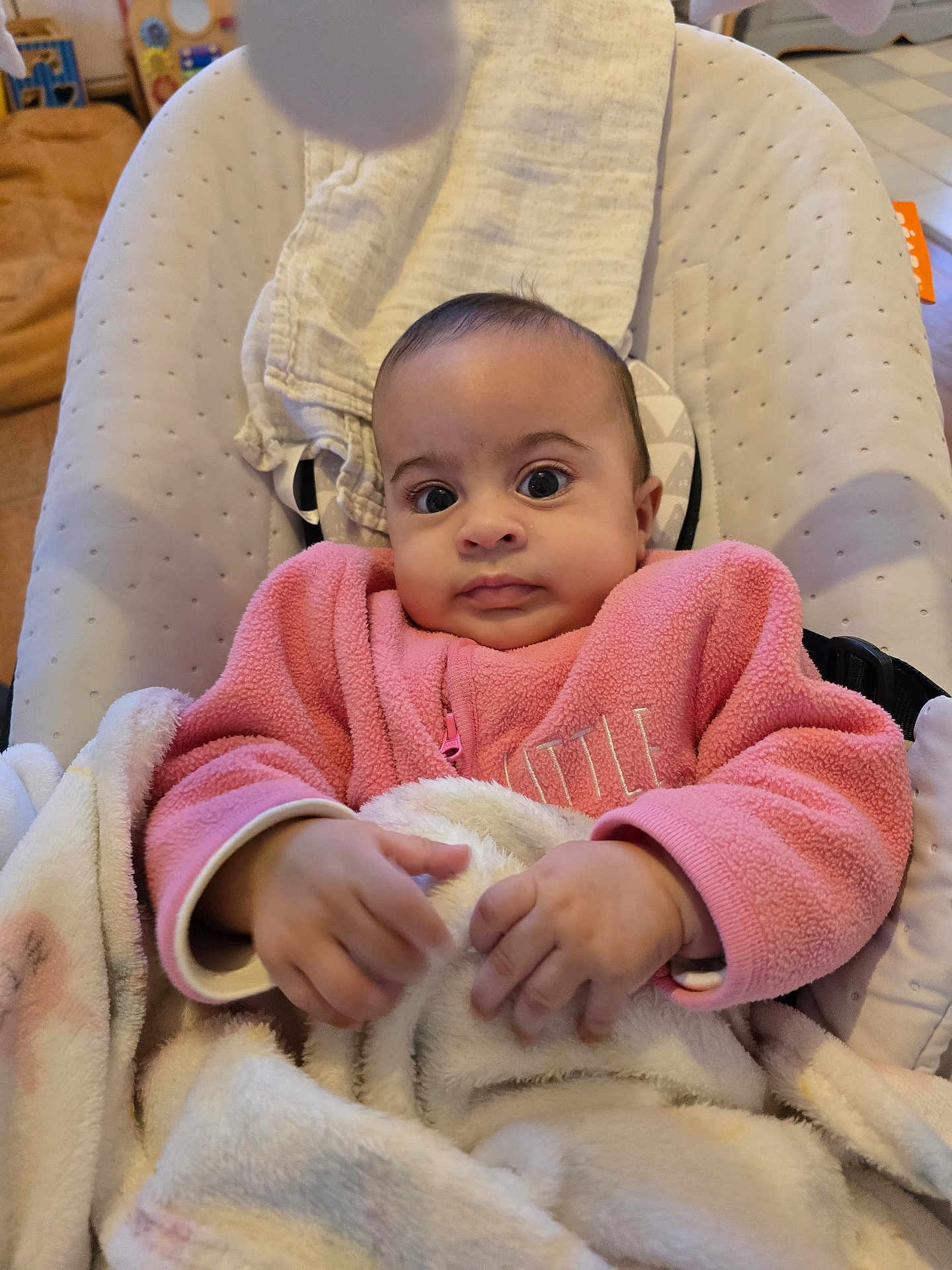 Leyna participe au concours pour gagner de l'argent avec cette photo : baby, infant, pink_jacket, blanket, baby_seat, indoor, child, cute, portrait, expression, cozy, hands, clothing, face, young, soft, comfort, seated, person, furniture