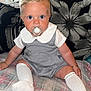 baby, child, pacifier, blue_eyes, socks, plaid_blanket, gray_outfit, white_collar, sitting, indoor, cushion, pillow, floral_pattern, striped_cushion, curly_hair, cute, portrait, person, infant, cozy