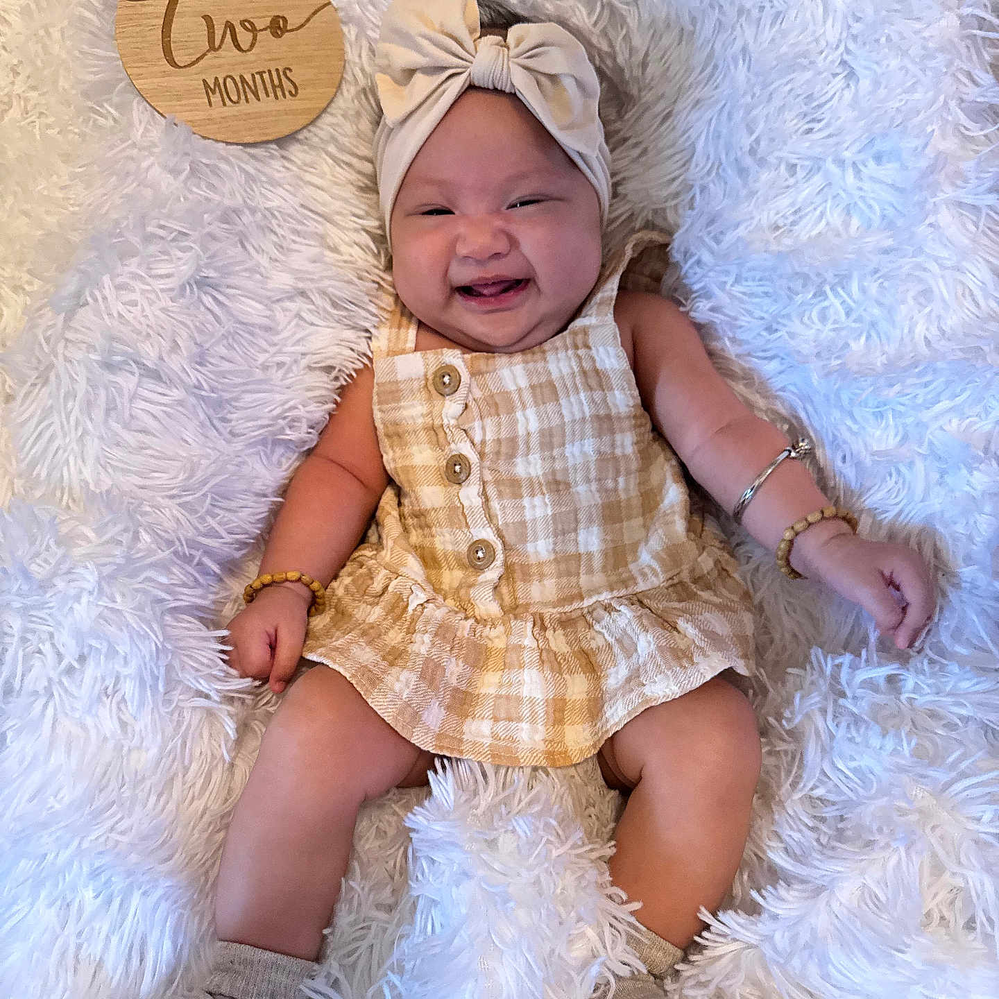 Ailah joined the competition — help win amazing prizes! arm_bracelet, baby, blanket, button, child, cozy, cute, dress, furniture, happy, headband, infant, lying_down, portrait, skin, smile, sock, soft_texture, two_months, wooden_sign