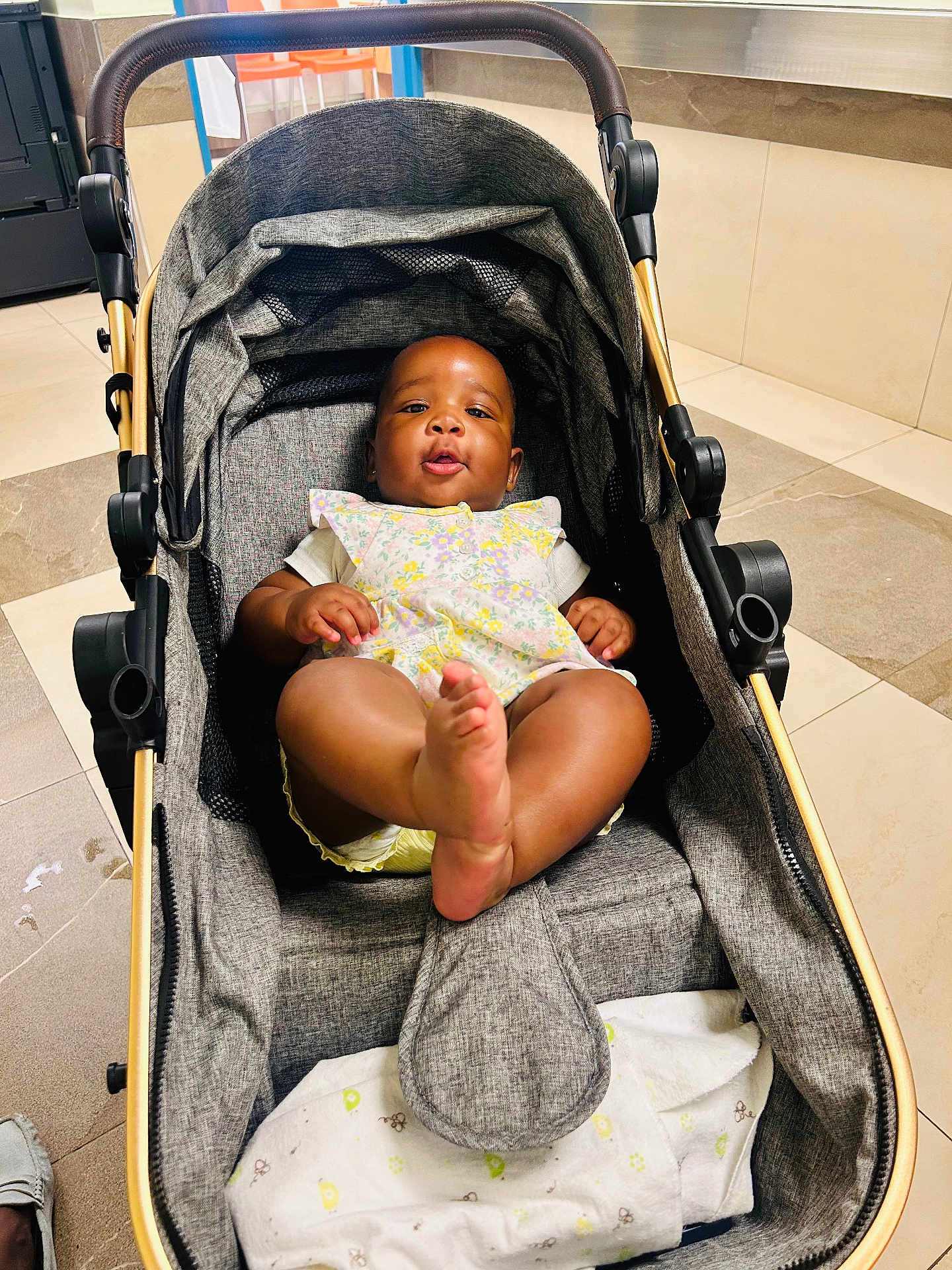 Anaya is registered to the contest to win money with this photo: baby, stroller, indoor, floor, tile, child, person, foot, clothing, fabric, blanket, seat, handle, playful, cute, infant, relaxing, modern, expression, kicking