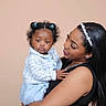 Sarai is registered to the contest to win money with this photo: baby, woman, child, portrait, indoor, holding, love, affection, smile, headband, curly_hair, black_hair, blue_clothing, casual, cute, family, mother, childcare, toddler, studio