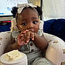 Sarai joined the competition — help win amazing prizes! baby, child, girl, infant, curly_hair, headband, white_bow, sitting, baby_chair, teddy_bear_pattern, hand_in_mouth, indoor, curious, cute, face, clothing, bracelet, furniture, window, couch