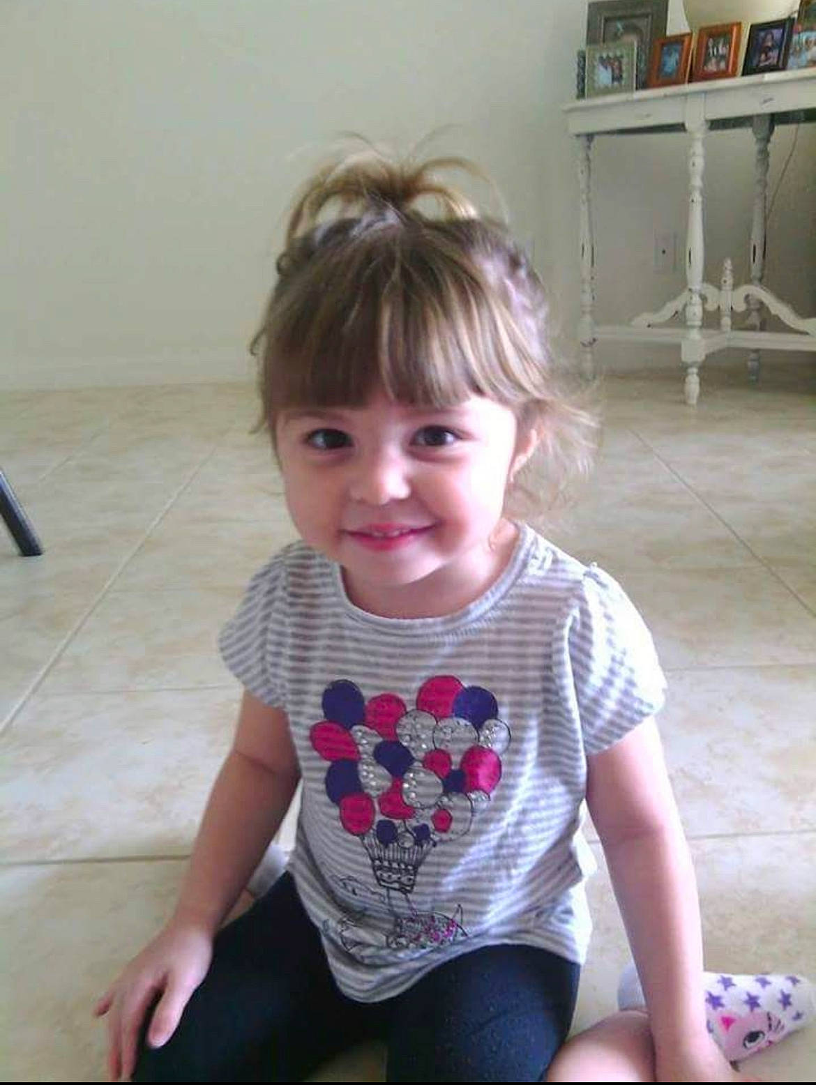 Adrianna is registered to the contest to win money with this photo: baby_toddler_clothing, bookcase, cheek, child, chin, facial_expression, flooring, hair, joint, joy, magenta, neck, pattern, person, shelf, shelving, sitting, skin, sleeve, t_shirt