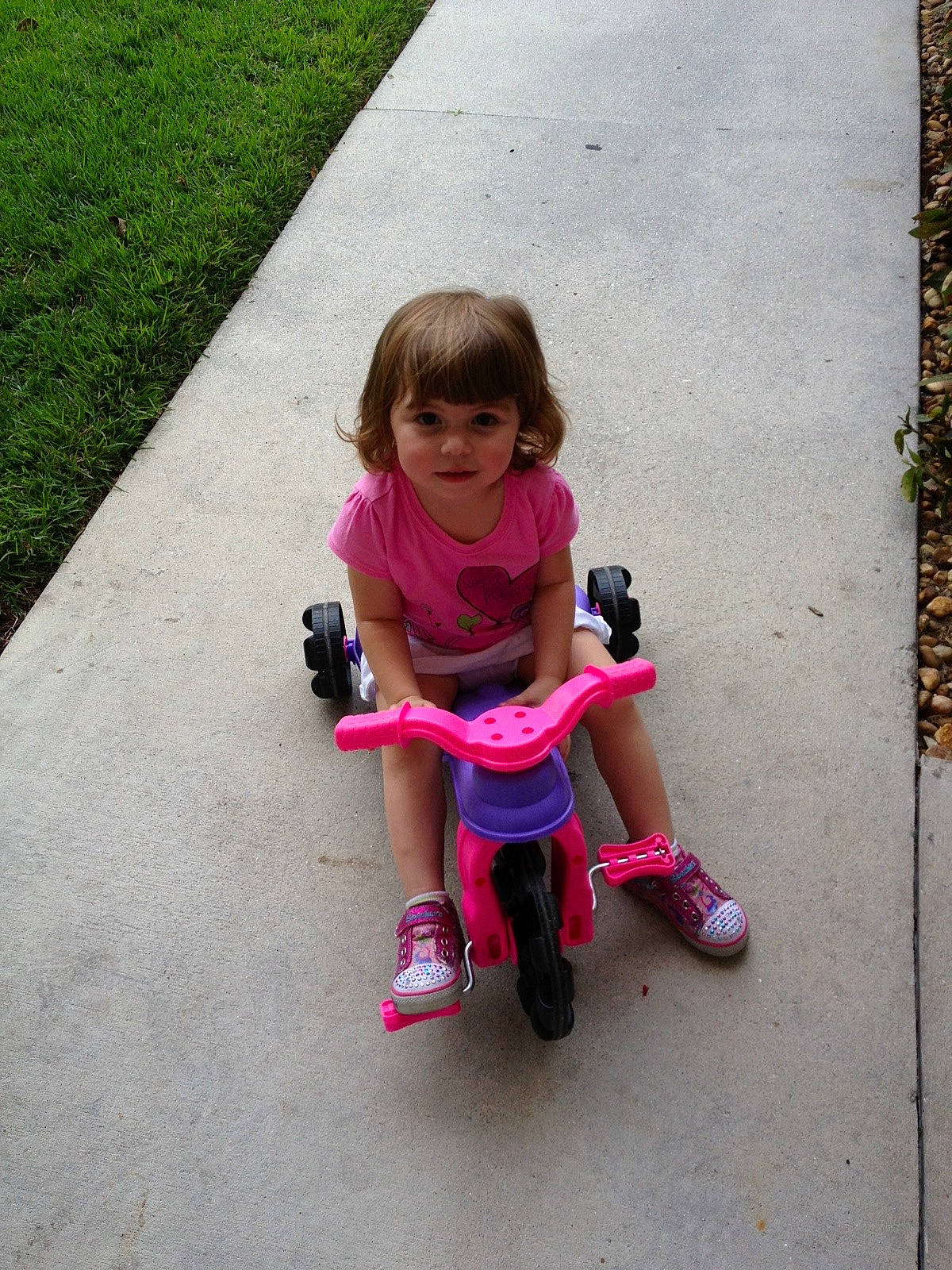 Adrianna is registered to the contest to win money with this photo: asphalt, baby_toddler_clothing, dress, face, footwear, fun, grass, happy, leg, leisure, magenta, mammal, person, pink, plant, recreation, road_surface, shoe, smile, toddler