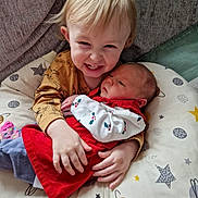 Sienna-Grace is registered to the contest to win money with this photo: toddler, baby, child, cushion, star_pattern, red_dress, mustard_shirt, smile, hugging, indoor, family, siblings, cute, happy, infant, young_children, portrait, couch, plush_surface, cozy